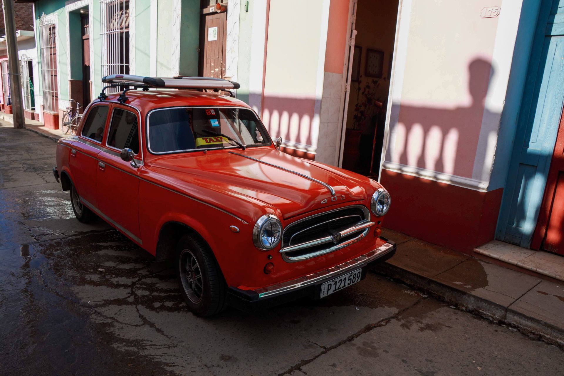 A classic red Peugeot 403 taxi parked by a colorful building, capturing vintage charm.