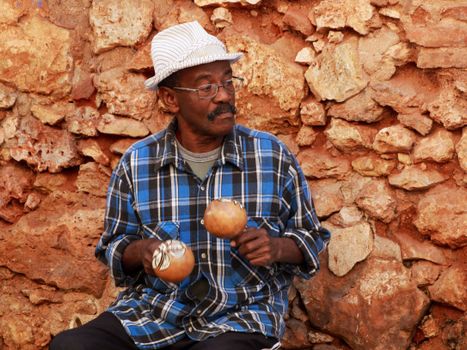 Senior street musician in a plaid shirt playing maracas against a rustic stone wall. — photo by Mehmet Turgut  Kirkgoz