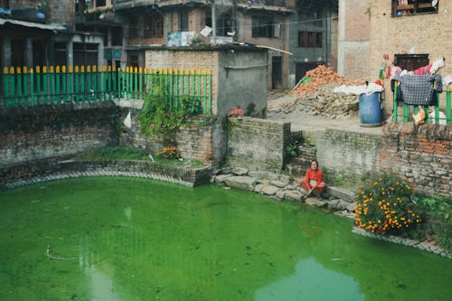 Elderly Woman Sitting by Water Pond in Town