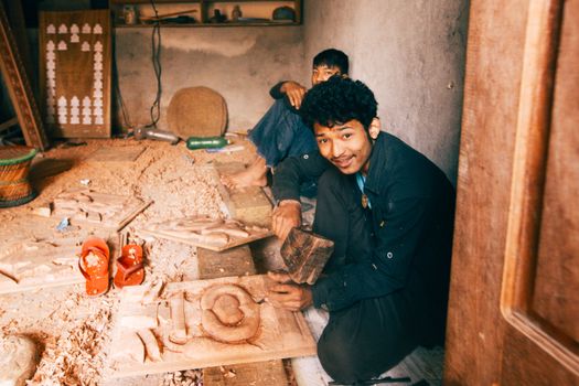 Two craftsmen working on wood carvings in a cozy workshop, surrounded by tools and wooden chips.