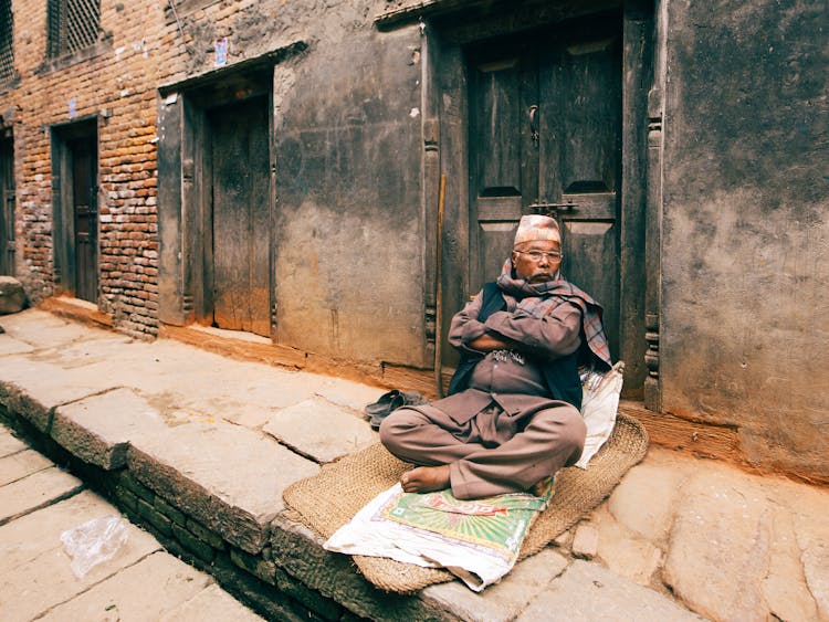 Elderly Man Sitting On Sidewalk In Front Of Door