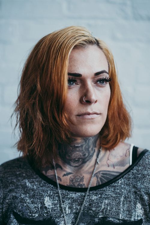 Free Close-up portrait of a woman with distinct tattoos and nose piercing standing indoors. Stock Photo