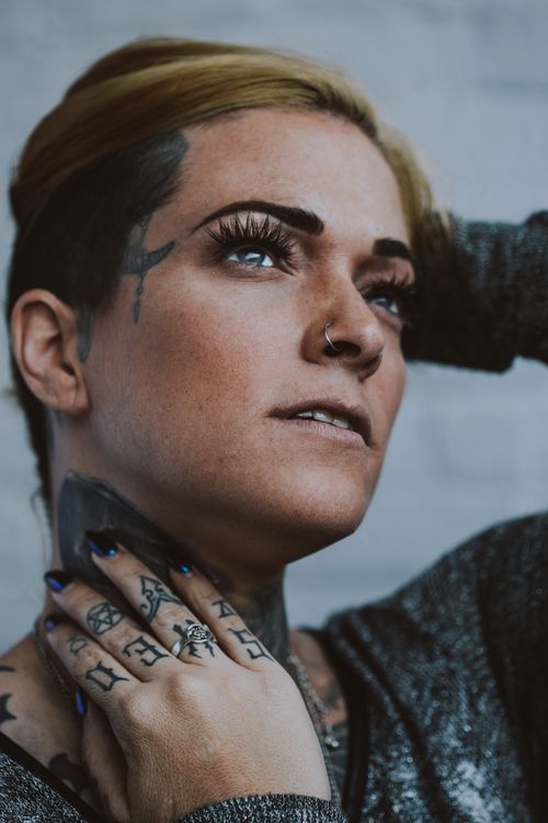 Free Close-up portrait of a tattooed woman with a nose piercing, looking thoughtful. Stock Photo