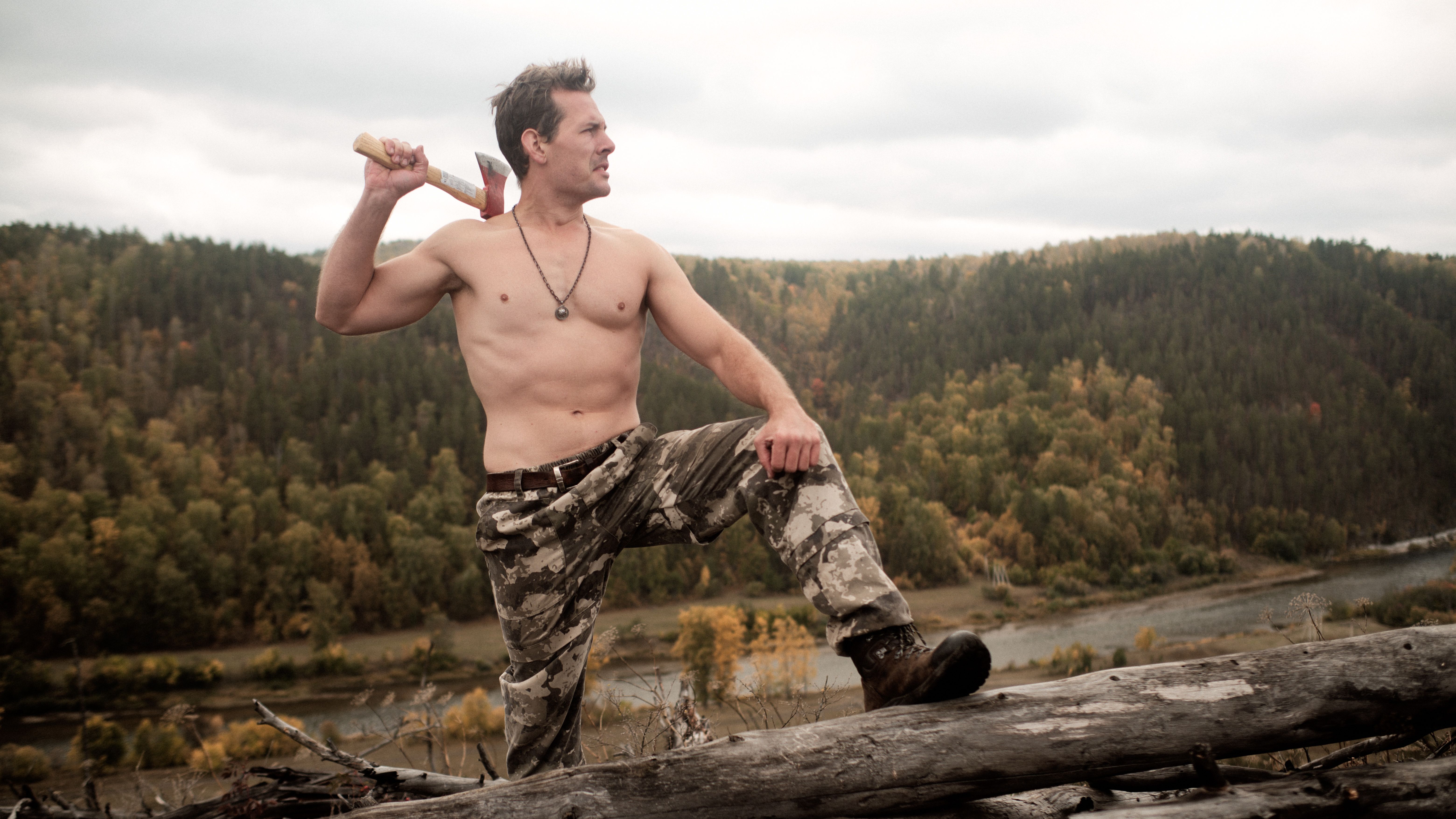 A muscular man with an axe in a scenic Russian forest, exuding strength and wilderness.