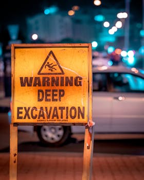 A caution sign for deep excavation in an urban environment at night.