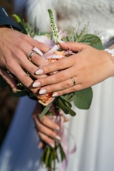 A close-up of a bride and groom's hands with wedding rings, holding a bouquet.