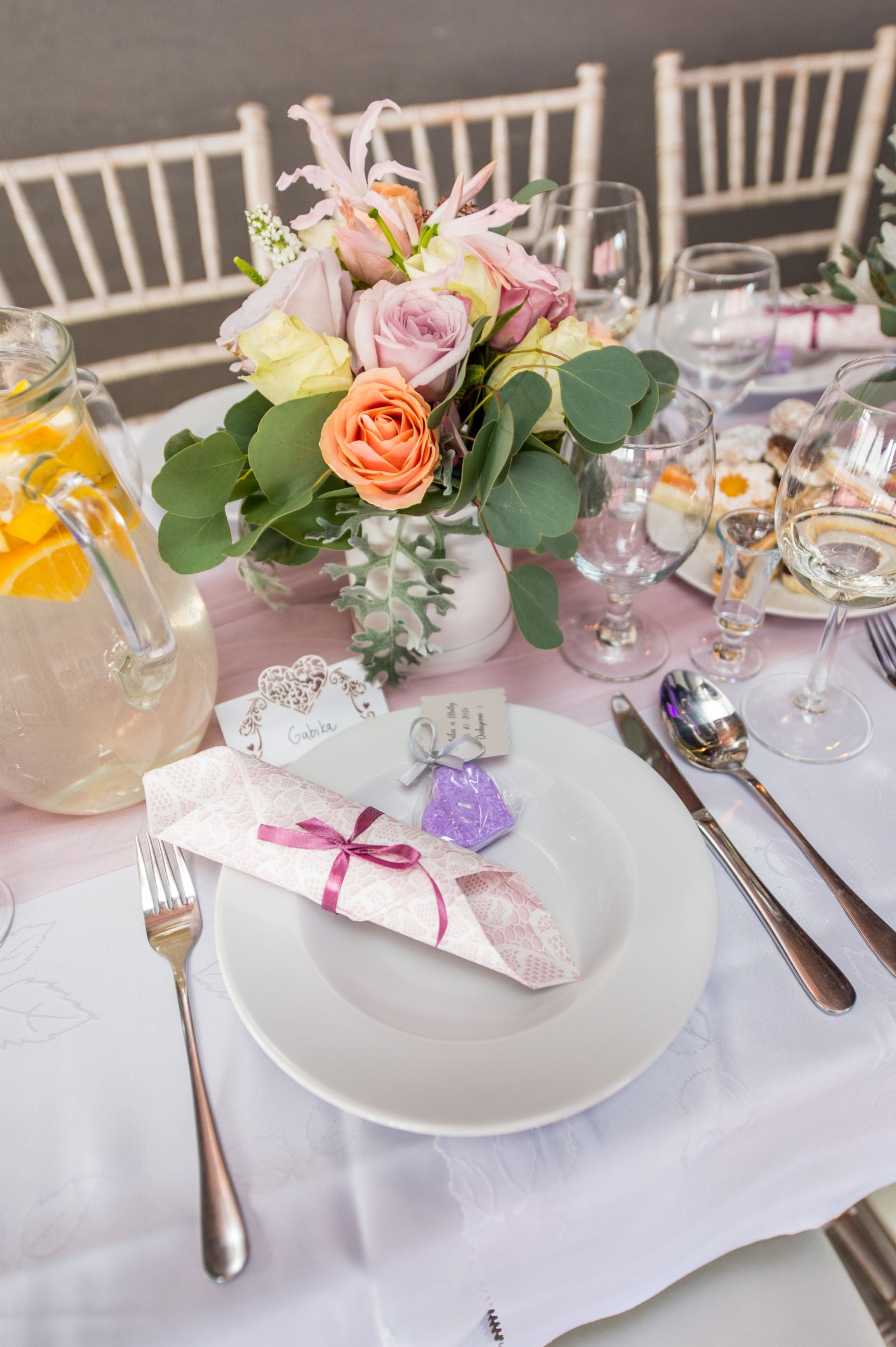 A practical event table set with flowers, plates, glasses, and a pitcher.