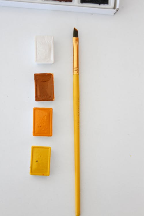 Yellow Paintbrush and Four Paints on a White Background
