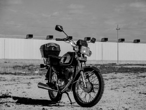 Free Black and white image of a classic motorcycle parked in an open area, showcasing vintage style. Stock Photo