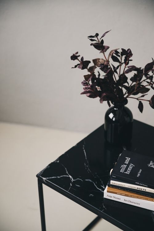 Free Elegant black vase with leaves on a marble table accompanied by stacked books. Perfect for minimalist, modern decor. Stock Photo