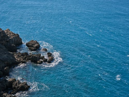 Free A tranquil rocky coastline with vibrant blue ocean waves crashing gently against the shore. Stock Photo