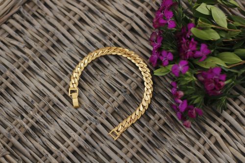 Free A stylish gold bracelet displayed on a wicker surface beside vibrant purple flowers. Stock Photo