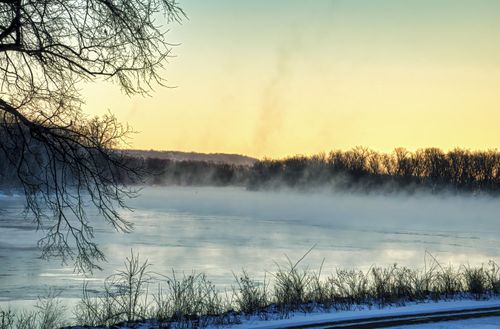 Free Peaceful winter scene of a frozen river and misty morning with leafless trees at sunrise. Stock Photo