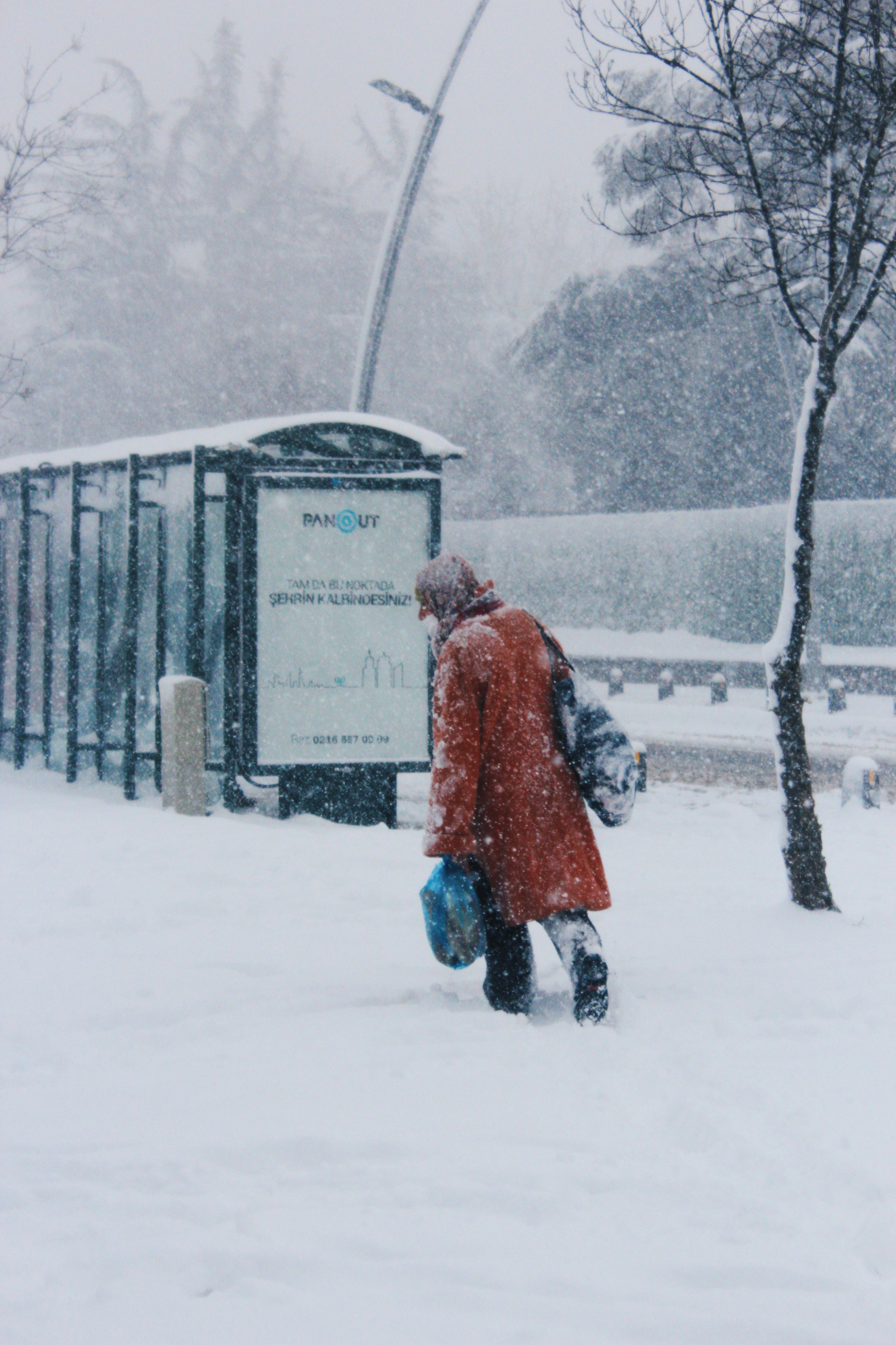 Person walking in snow near Istanbul bus stop during winter weather.