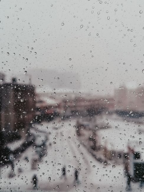 Raindrops on a window with a blurred snowy view of İstanbul city street.