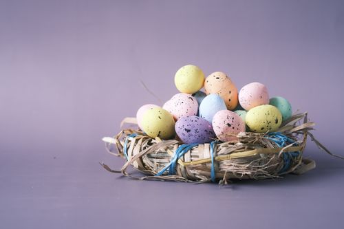 Free Vibrant pastel Easter eggs in a woven nest against a soft purple background. Stock Photo