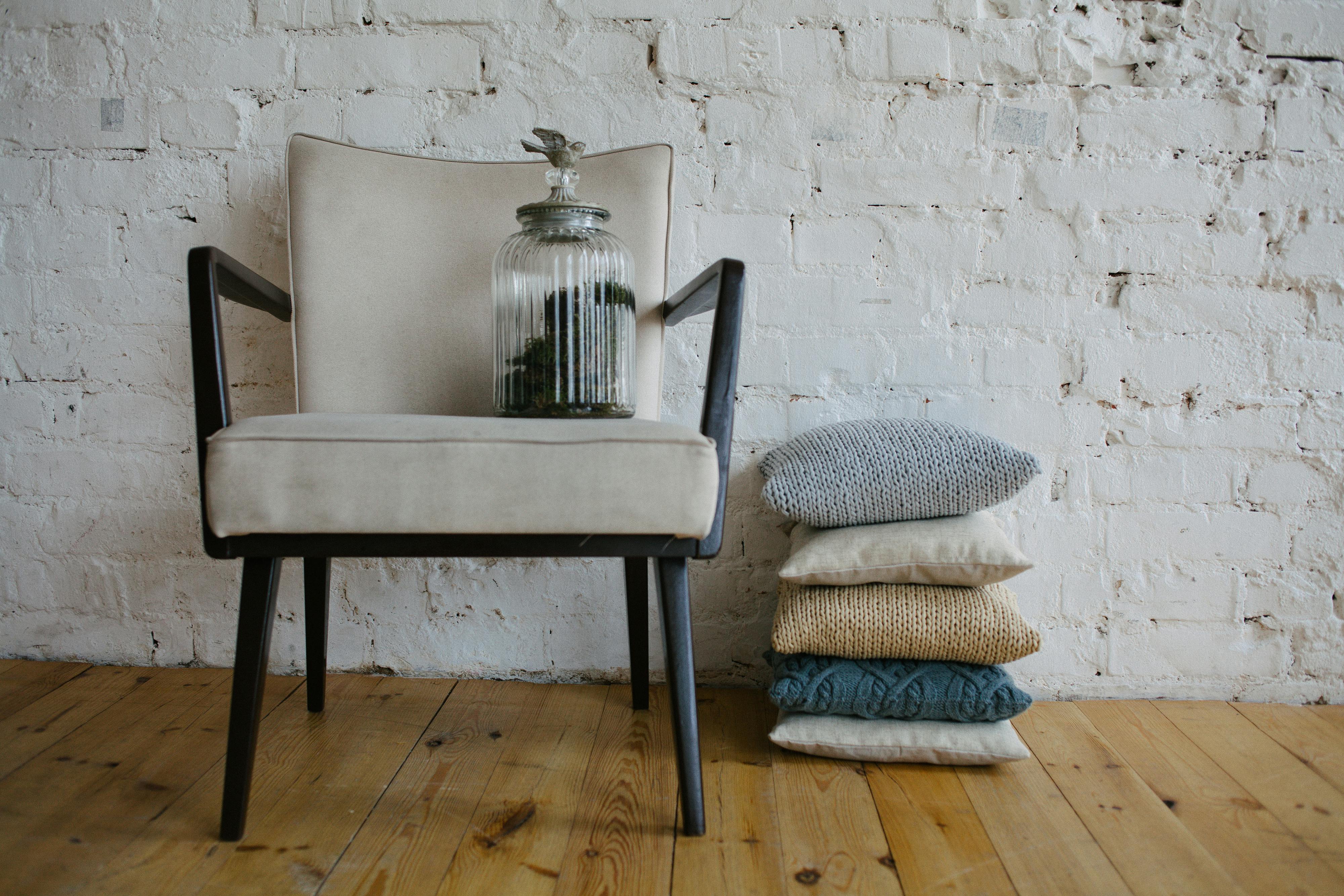 Minimalist white room with a chair, cushions, and a glass jar. Perfect for cozy home decor inspiration.