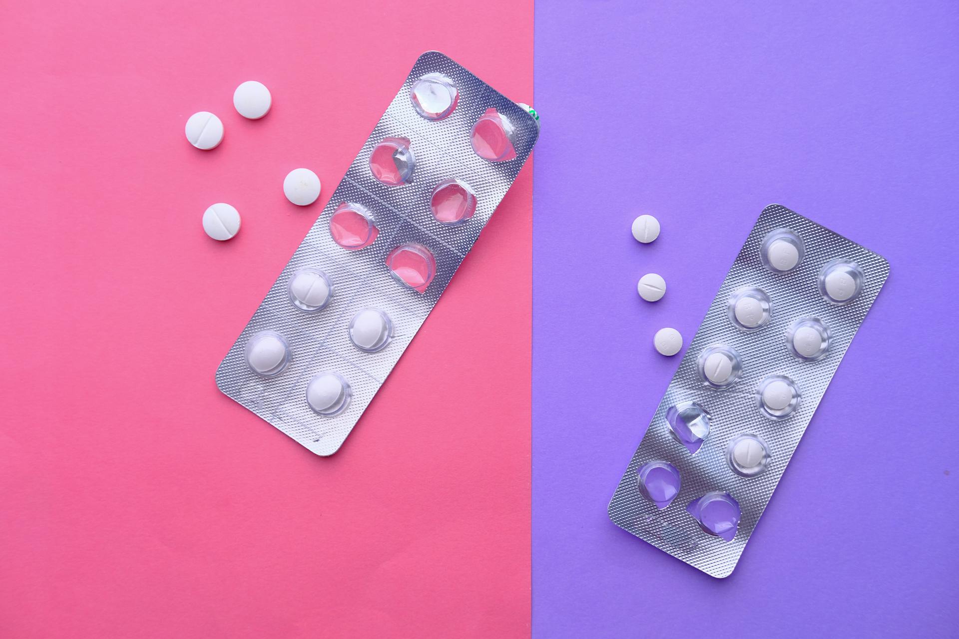 Top view of blister packs and pills on a vibrant pink and purple background.