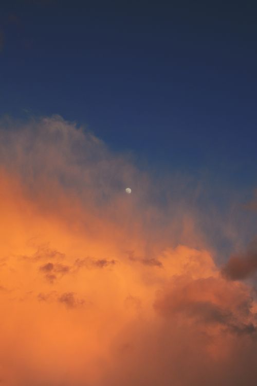 Free A vivid sunset sky with a visible moon amidst vibrant orange clouds. Stock Photo