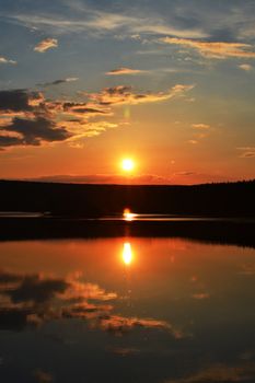 Tranquil sunset casting reflections on a calm lake, with vibrant hues in a peaceful setting.