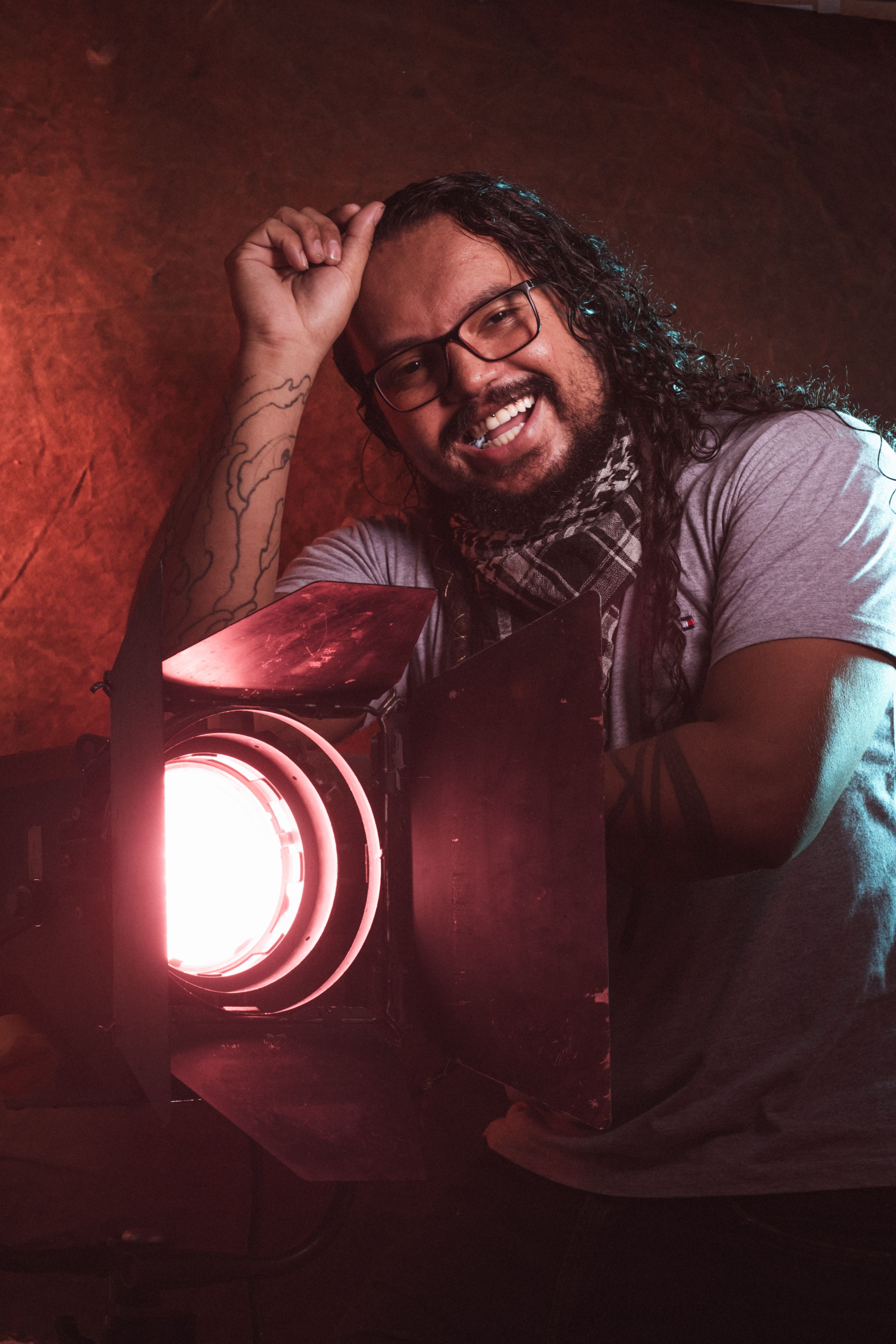A cheerful man with eyeglasses poses under pink studio light, showing vibrancy and creativity.
