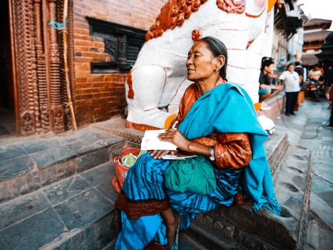 Elderly woman sitting on temple steps, reading in a vibrant urban scene.