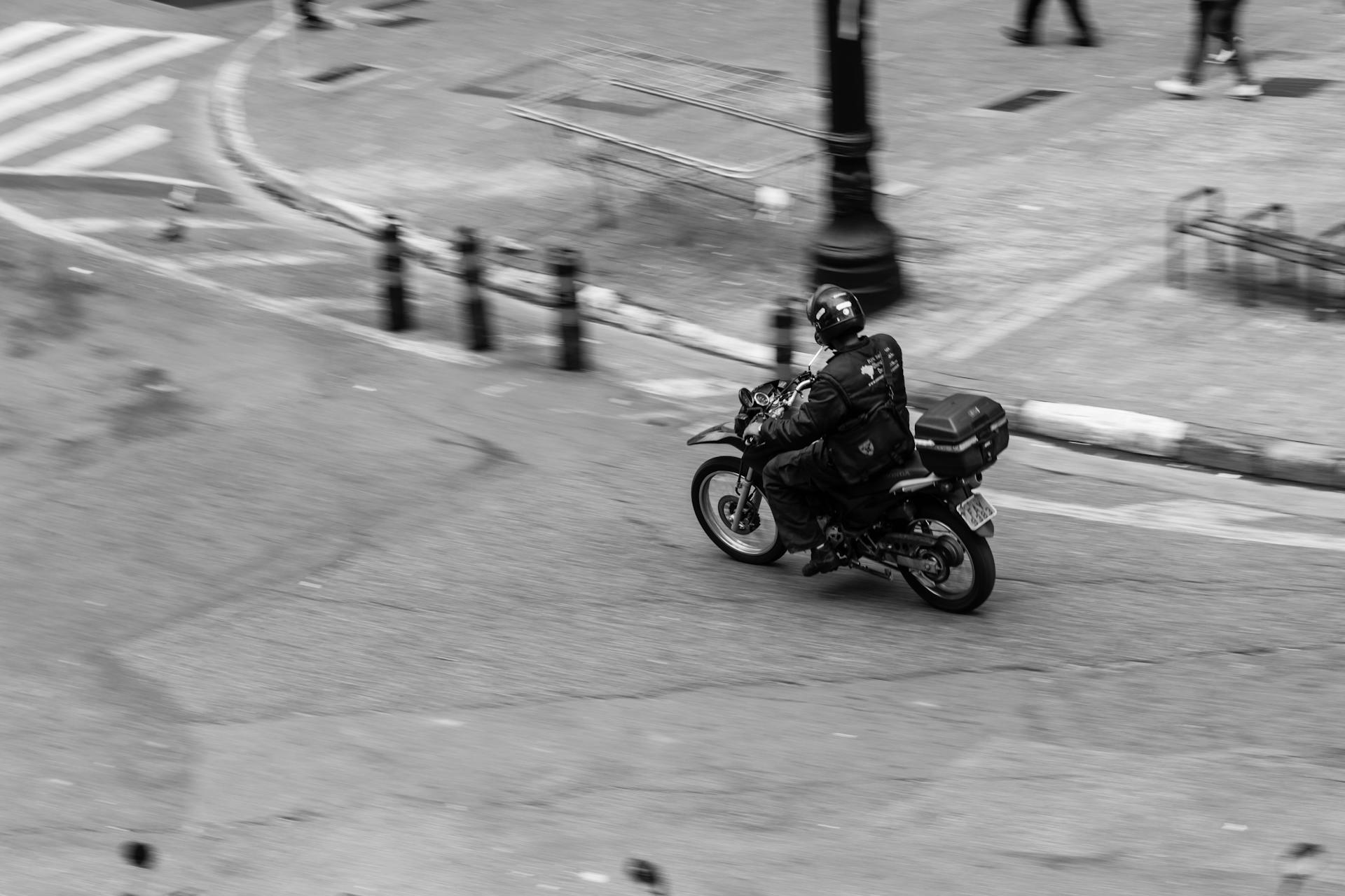 A motorcycle rider speeds through a city street captured in monochrome.