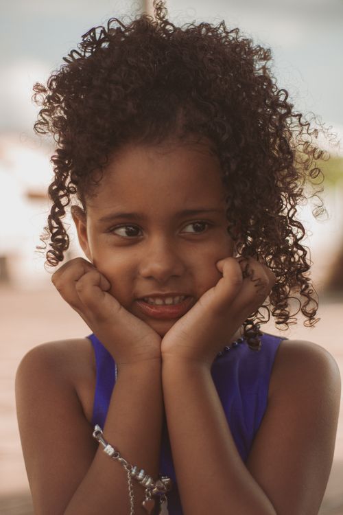 Free Charming portrait of a young girl with curly hair resting her chin on her hands, outdoors. Stock Photo