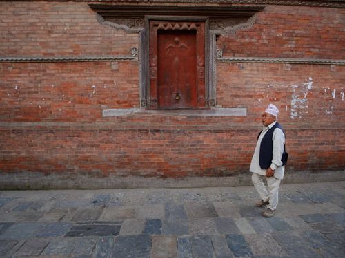 Free A senior man walks by a historical red brick wall with a wooden door. Stock Photo