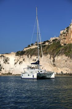 A serene sailboat anchored by the cliffs of Vieste, Italy on a sunny day.