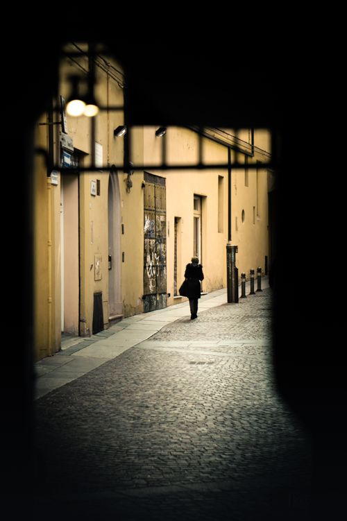 Free A solitary figure walks down a lit street in Bologna, Italy, capturing urban solitude. Stock Photo