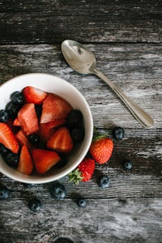 一碗新鲜草莓、蓝莓和西瓜片摆放在质朴的木制桌面上，非常适合食品摄影