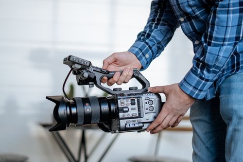 Free Close-up of person operating a professional video camera indoors, wearing flannel. Stock Photo