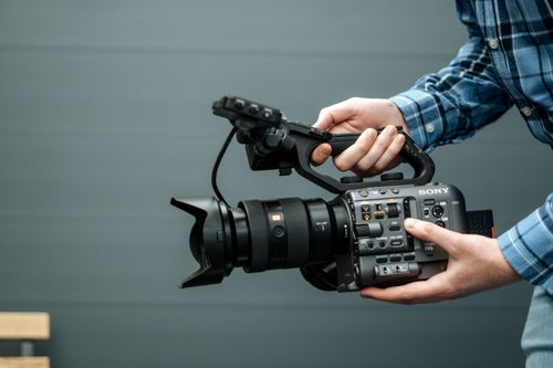 Free Close-up of a person handling a professional video camera indoors, emphasizing modern film equipment. Stock Photo