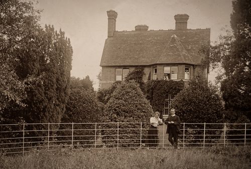 Free Nostalgic sepia photo of an English countryside farmhouse with people outside and greenery. Stock Photo