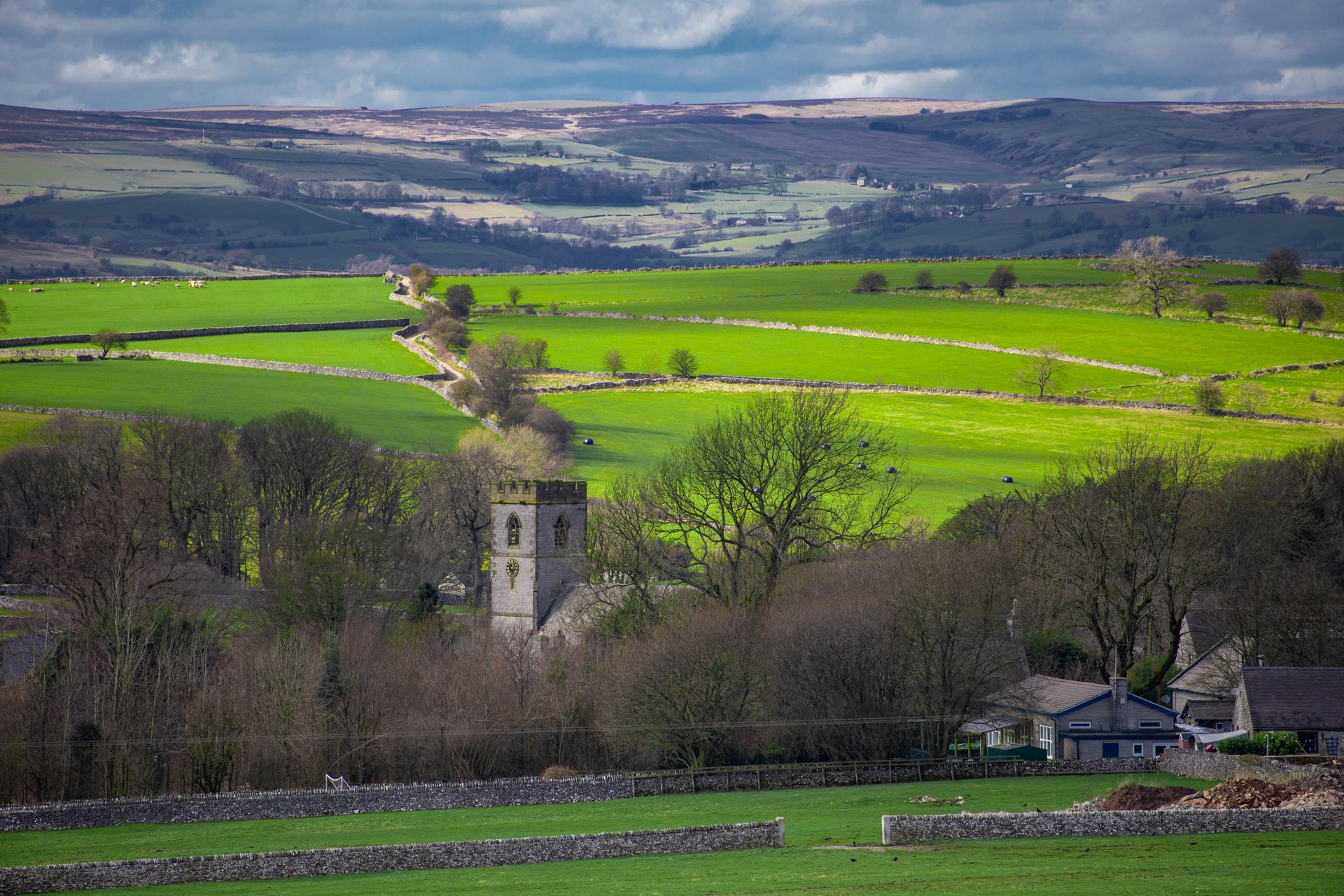 Peaceful rural landscape featuring lush green fields and a historic church tower under a cloudy sky.