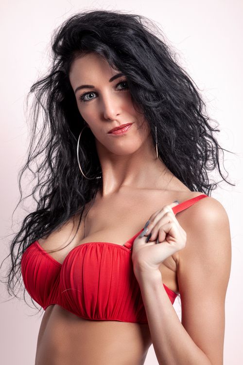 Free Studio portrait of a woman wearing a red brassiere and hoop earrings, exuding confidence. Stock Photo