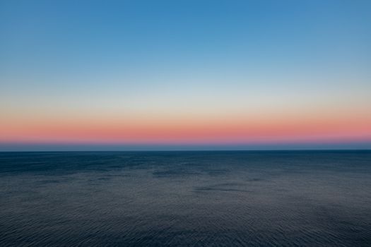 A serene view of the ocean at sunset with vibrant sky hues and calm waters.