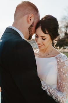 A loving moment captured between newlyweds embracing outdoors with natural sunlight.
