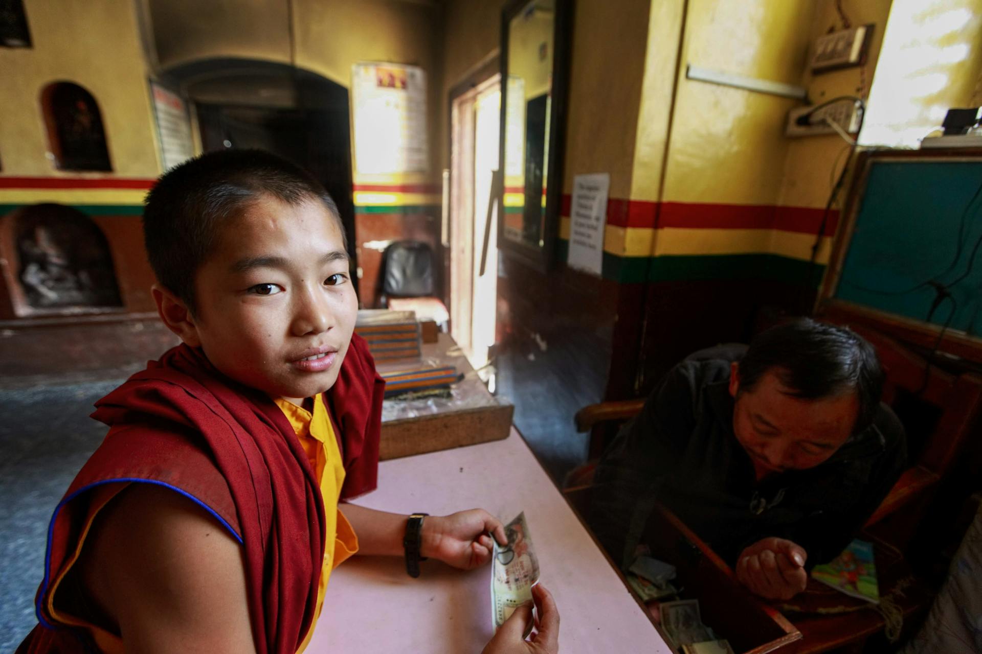 A young monk holding money inside a vibrant temple, immersed in education.