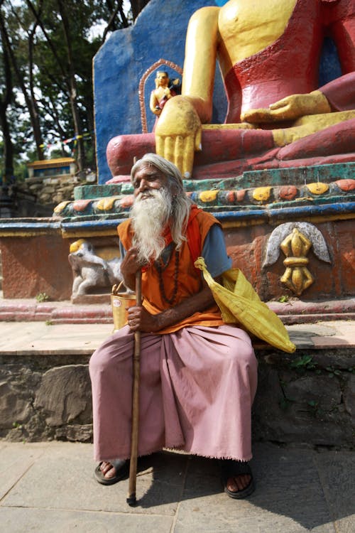 Elderly Monk Sitting in Front of a Statue 