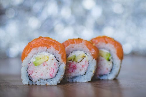 Drie hapjes gezonde 'California Maki' sushi naast elkaar op een houten tafel.