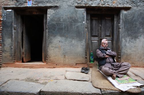 Free Senior man in traditional clothing sits cross-legged outside a rustic building. Stock Photo