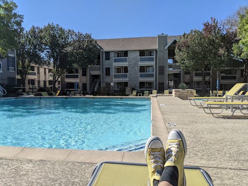 A Person in Yellow and White Sneakers is Sitting Near Swimming Pool