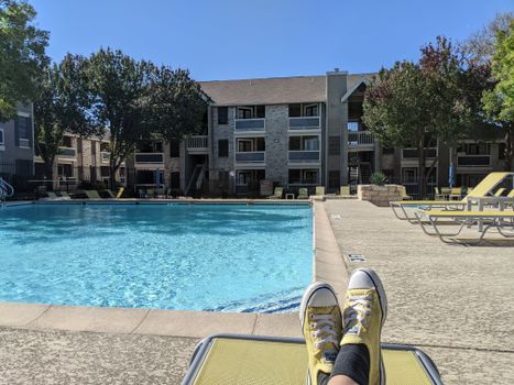 Person lounging by a pool in a sunny apartment complex, enjoying summer relaxation.