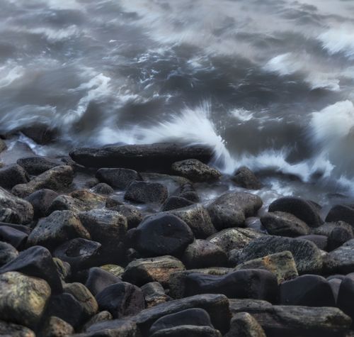 Free Dramatic stormy sea waves crashing against dark, rugged rocks on a coastal shore. Stock Photo