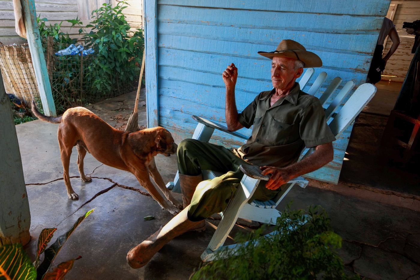 A senior man in a hat resting on a country porch beside his dog