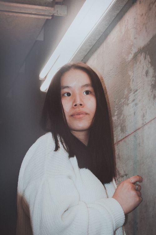 Free A thoughtful woman stands in industrial lighting against a concrete wall, creating a moody atmosphere. Stock Photo