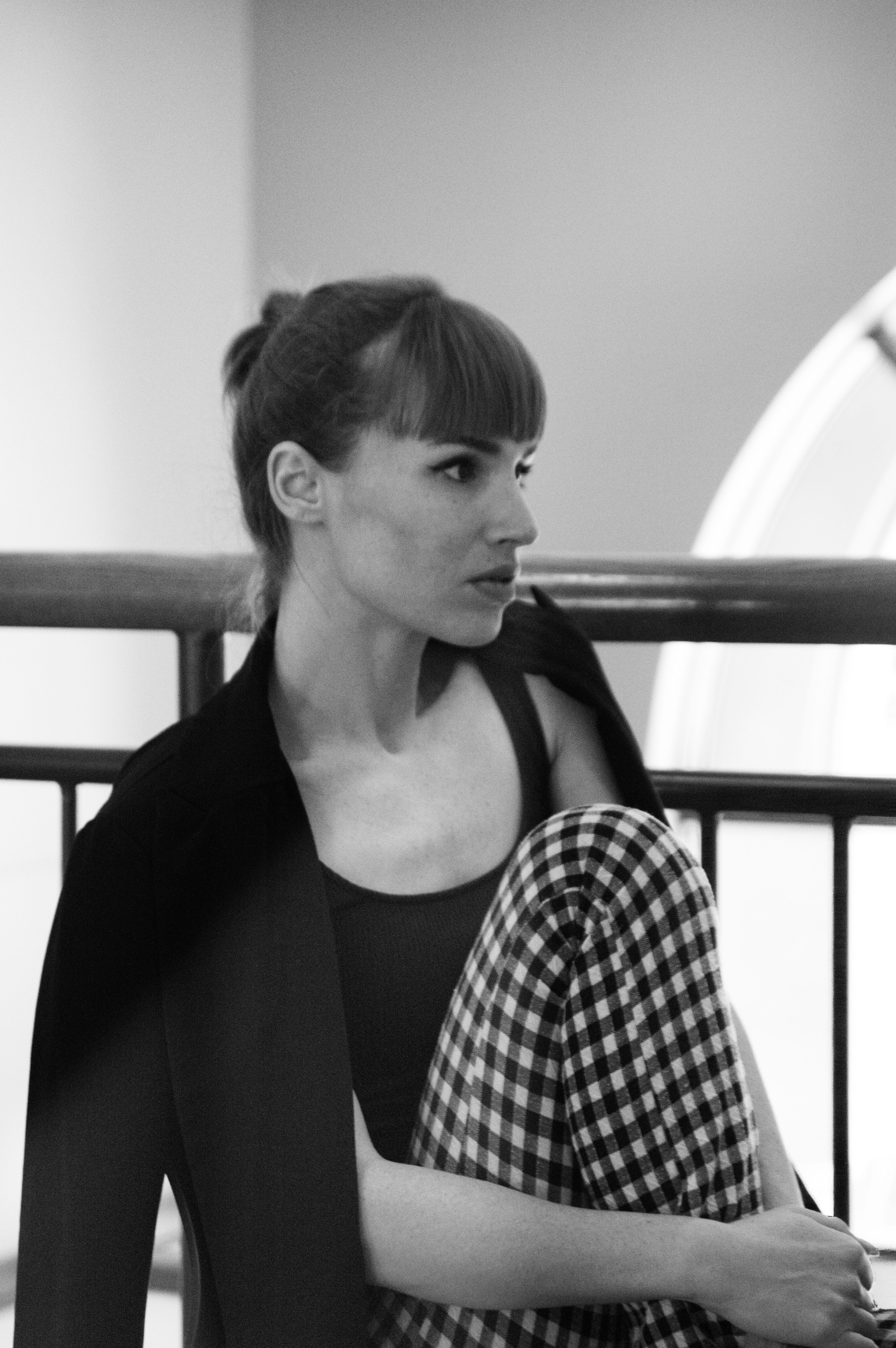 Elegant black and white portrait of a woman sitting indoors, wearing plaid pants and a blazer.