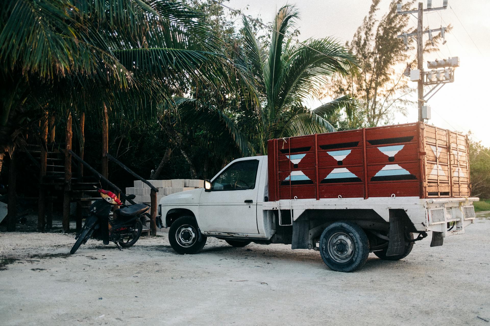 A utility truck parked by palm trees on a sandy beach in Cozumel, Mexico at sunset.